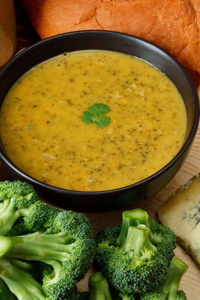 A close-up view of creamy broccoli and Stilton soup with a side of crusty bread on a dark background.