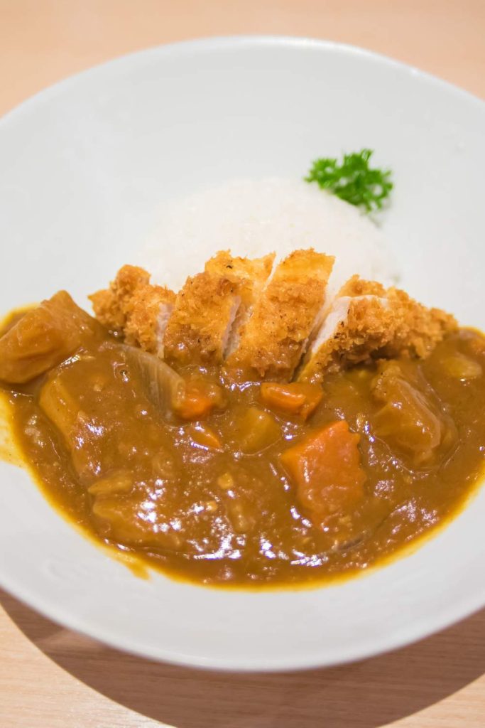 Close-up of katsu curry beside rice in a white bo