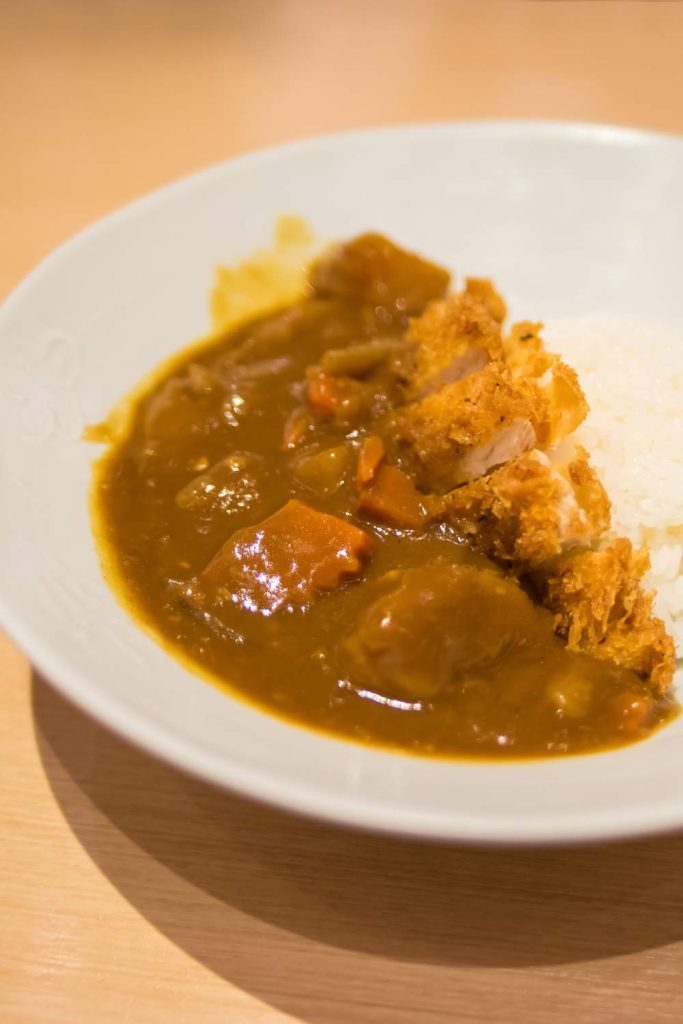 A bowl of katsu curry with rice and a breaded chicken cutlet on top.