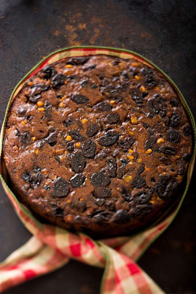 A full Christmas fruit cake with a rich raisin topping on holiday-themed fabric.
