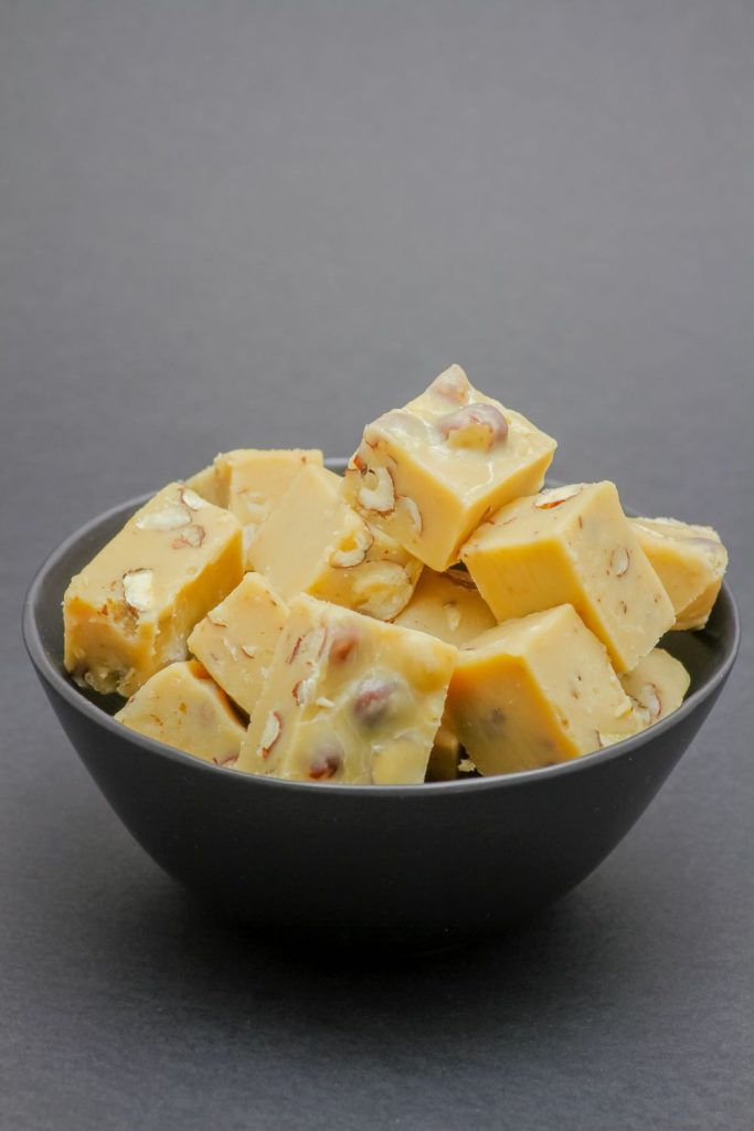 Bowl filled with pieces of light-colored nut fudge on a dark background.