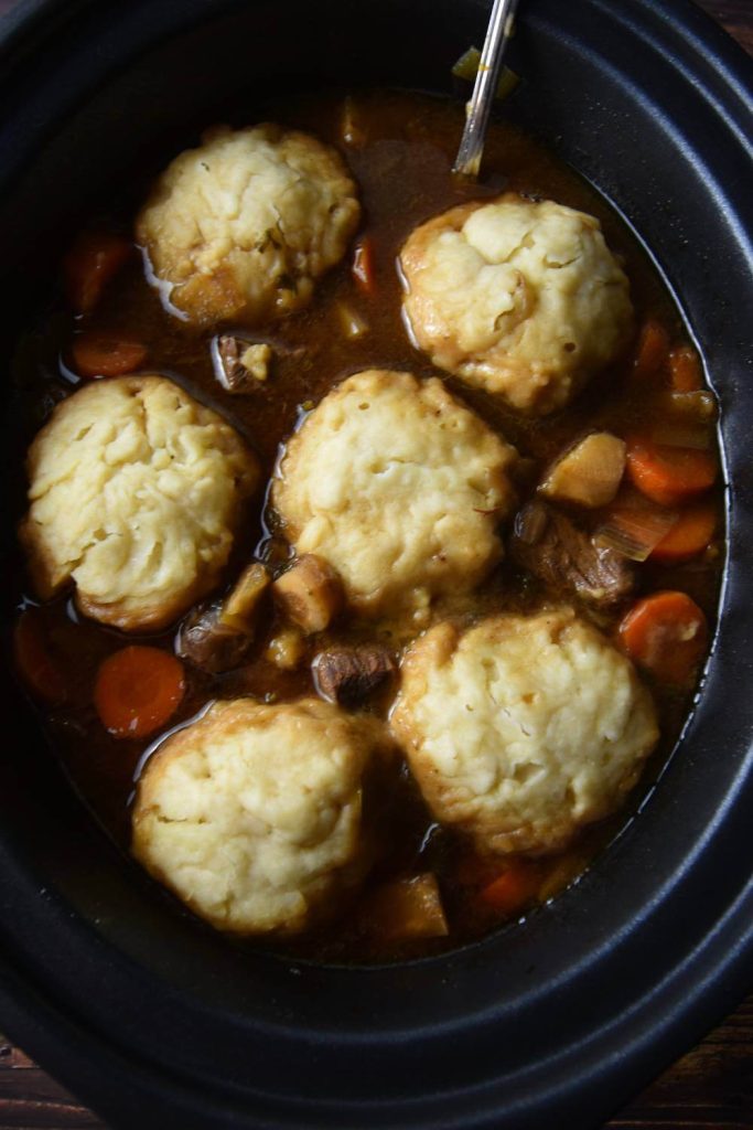 A black slow cooker filled with stew and several fluffy Aunt Bessies dumplings on top