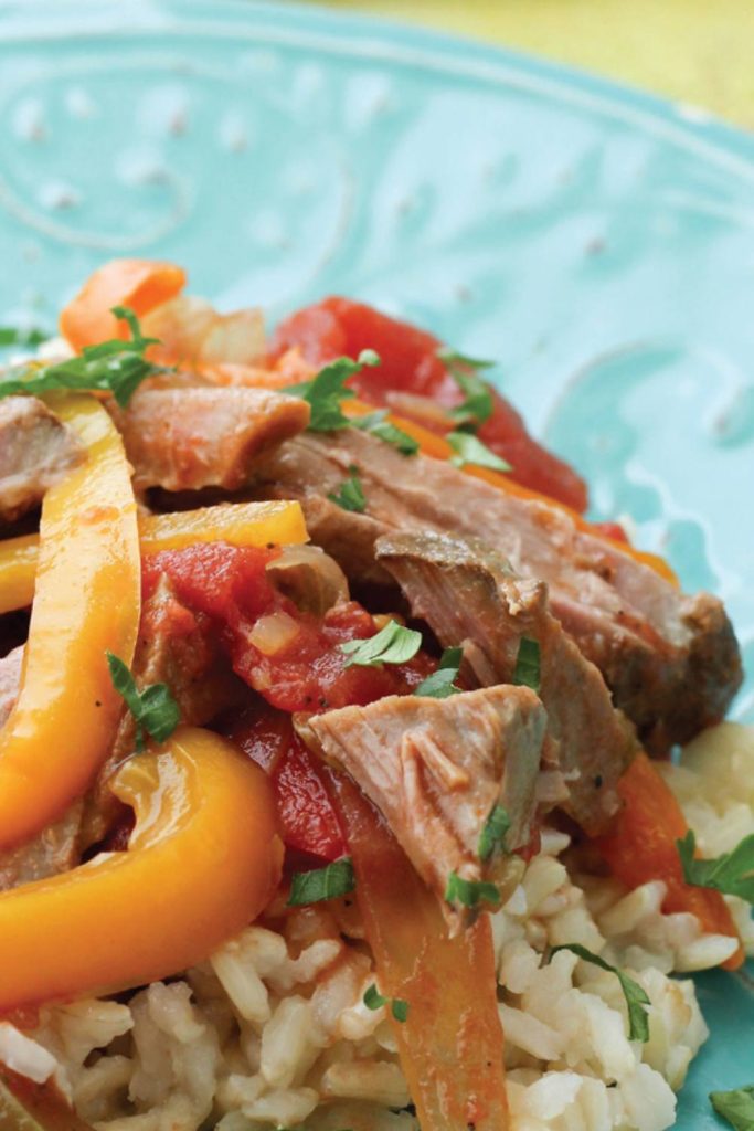 Close-up of slow-cooked pepper steak with tomatoes and parsley on a blue plate.