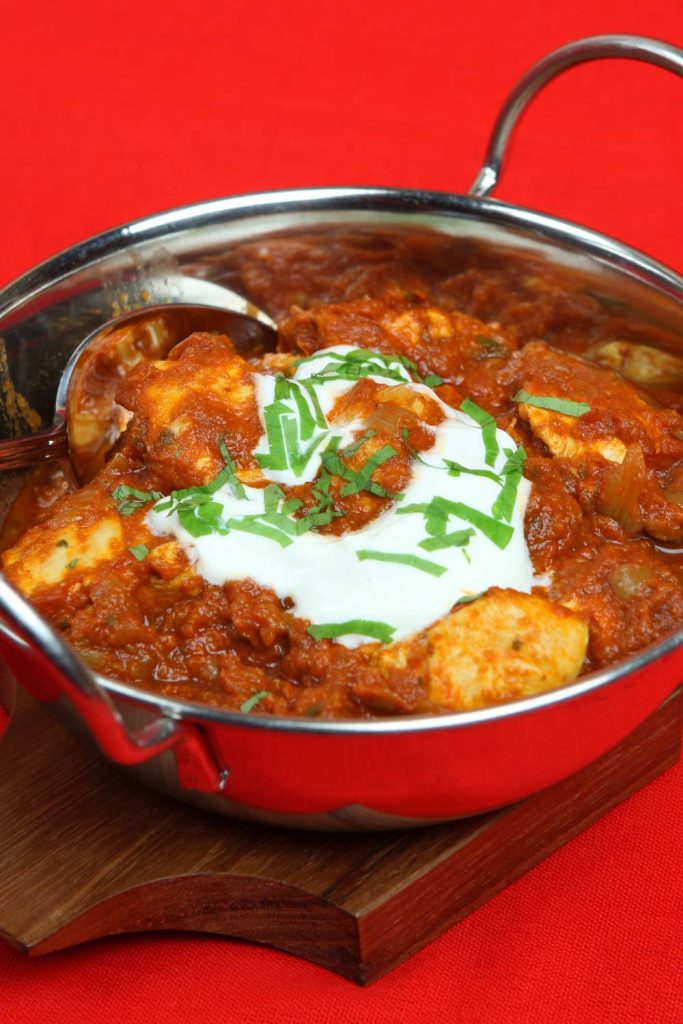 Chicken Madras in a pot with yogurt and green herbs, on a red background.