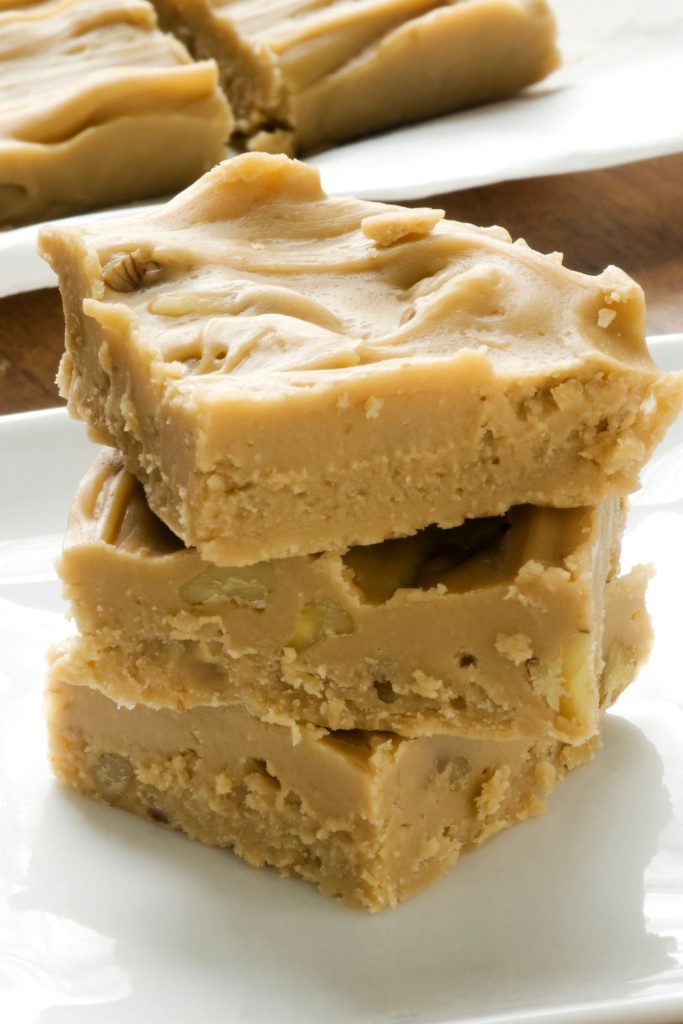 Stack of creamy fudge with nuts in a light color on a white plate.
