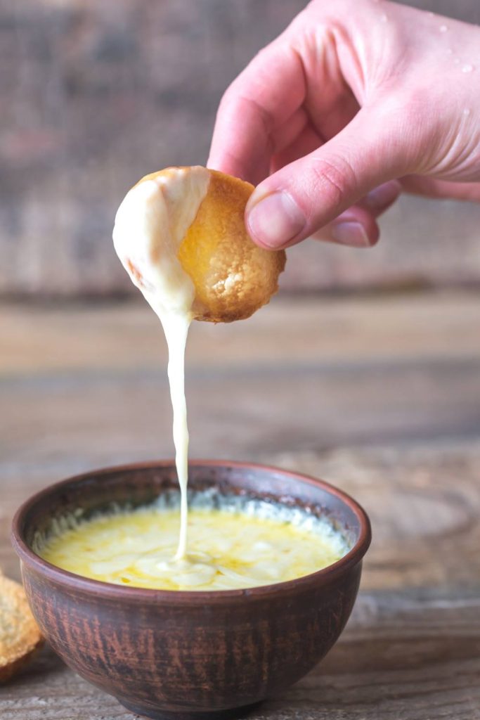 Hand dipping bread into a bowl of queso.