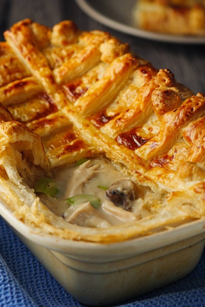 A close-up of a chicken and leek pie with a flaky crust in a baking dish.