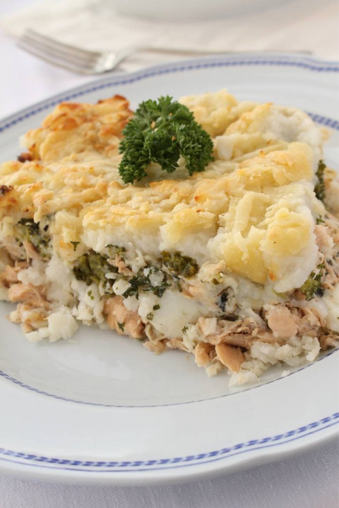 Golden-brown fish pie served on a plate with a side of parsley.