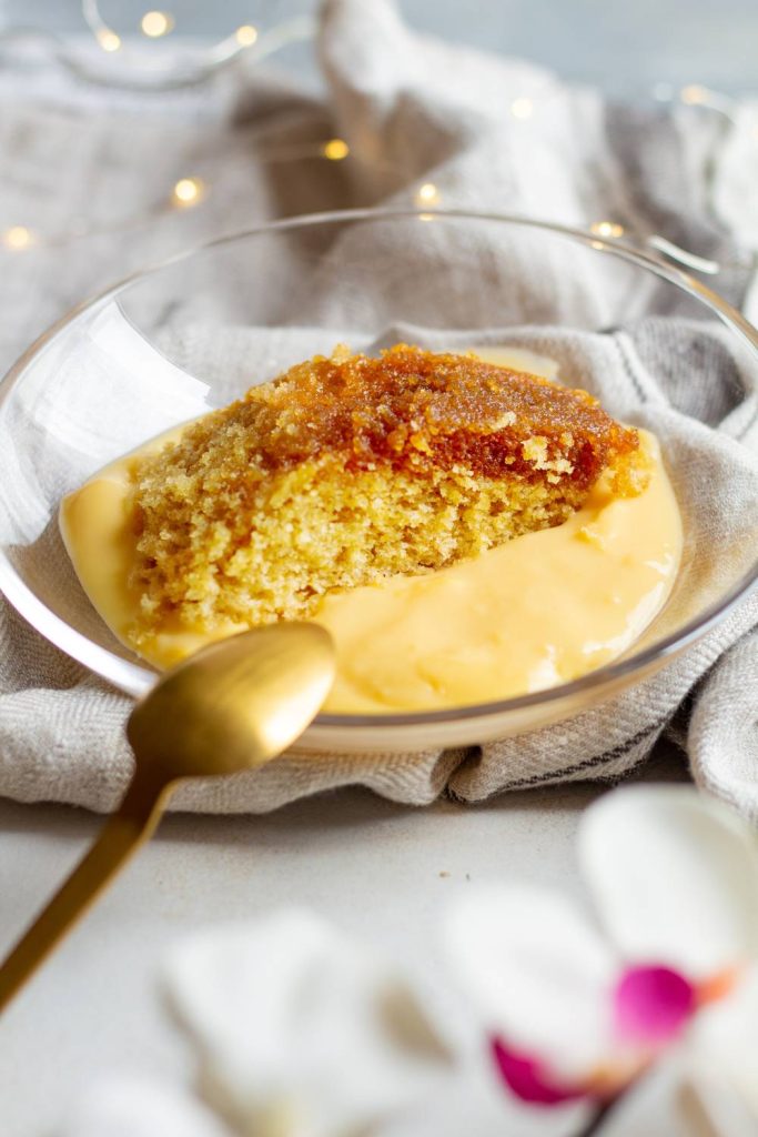 A slice of golden treacle sponge with custard in a clear bowl.