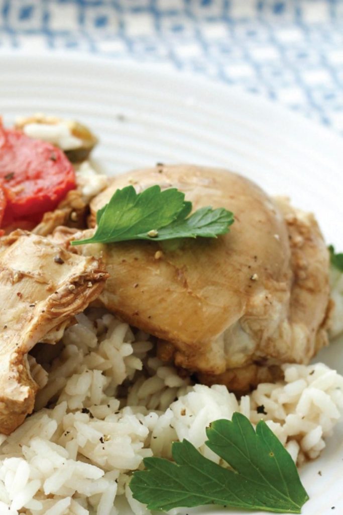 A close-up of tender slow-cooked chicken atop seasoned rice, garnished with fresh parsley.