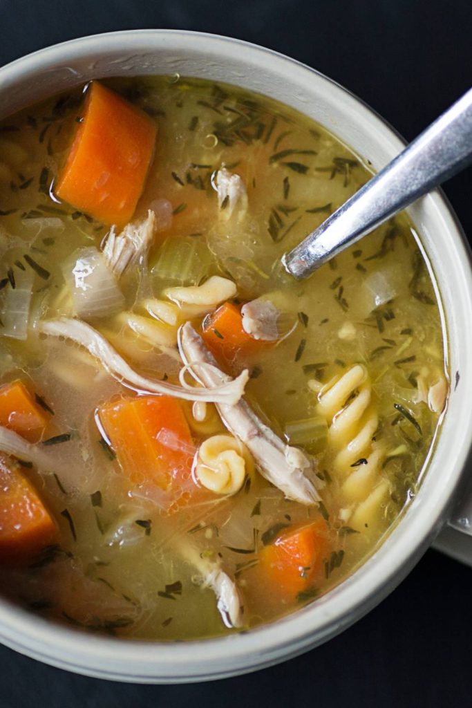 Steaming chicken soup in a white bowl with carrots and pasta, made in a slow cooker.