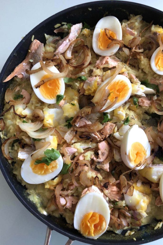 A skillet of kedgeree with flaked fish, boiled eggs, and crispy onions, ready to be served.