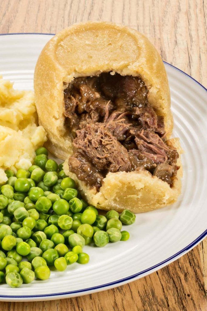 A complete meal featuring steak and kidney pudding with mashed potatoes and peas on a plate.