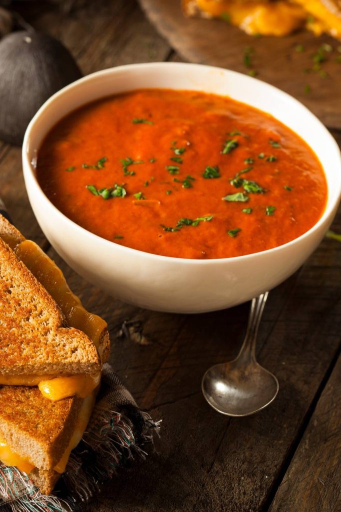 Homemade tomato soup in a white bowl with a grilled cheese sandwich.
