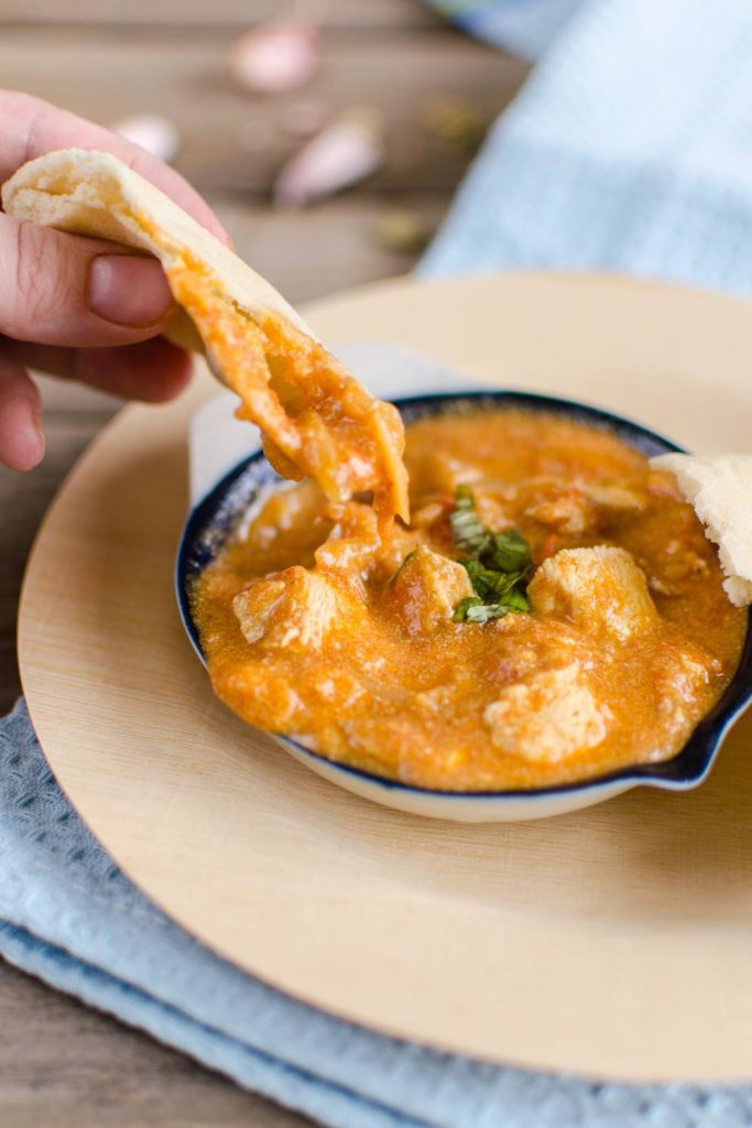 Scooping chicken balti with naan from a blue-rimmed bowl.