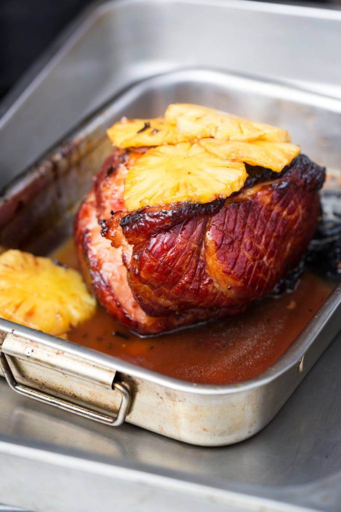 Ham with pineapple slices in a roasting pan with juices.