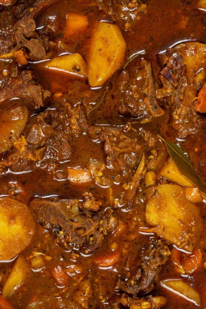 A pan full of rich and hearty slow cooker goat stew with potatoes and carrots.