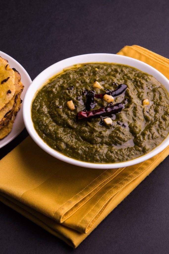 White bowl of lamb saag on a dark background with golden cloth.