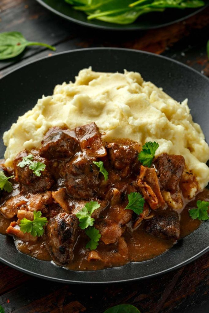 A comforting liver and bacon casserole served with creamy mashed potatoes and garnished with parsley.