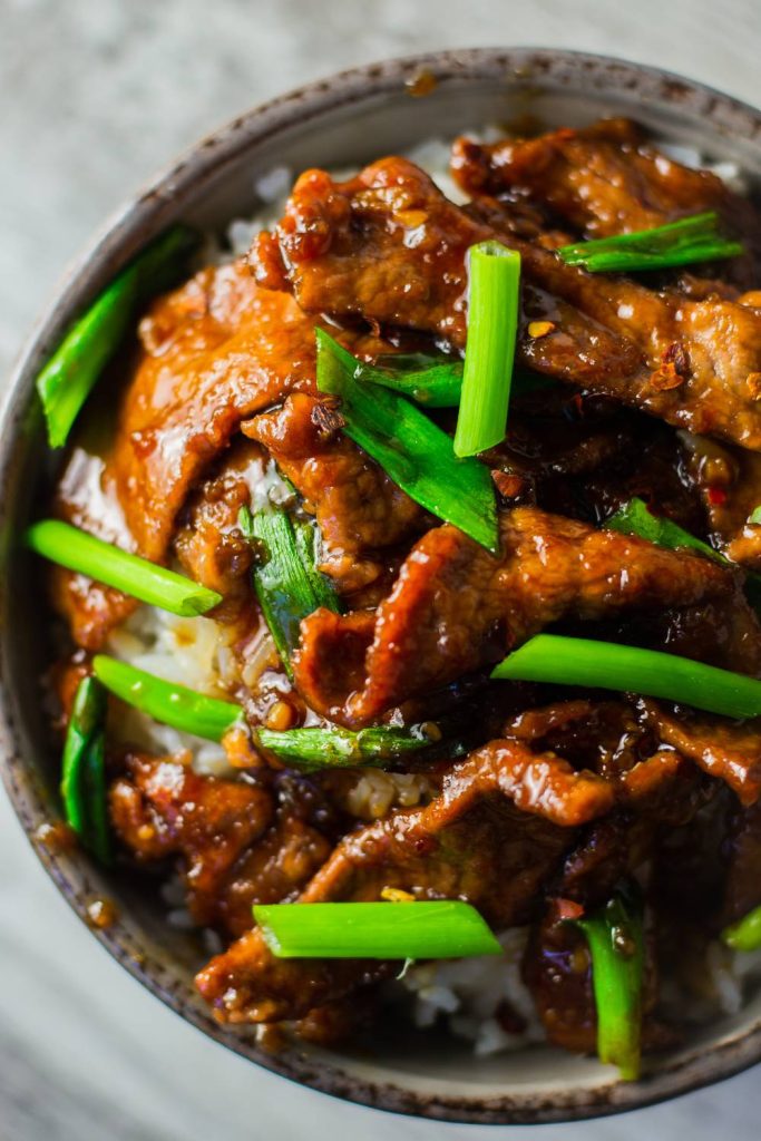 A bowl of Slow Cooker Mongolian Pork over rice garnished with green onions.