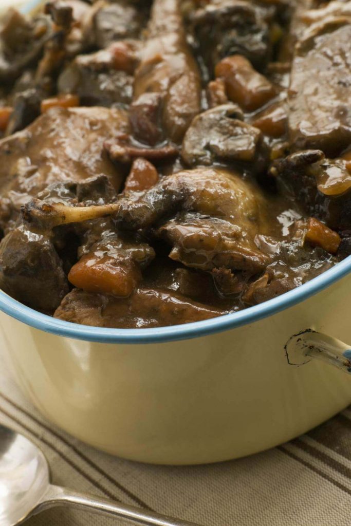 A steaming pheasant casserole in a pot, simmered in red wine sauce with vegetables.