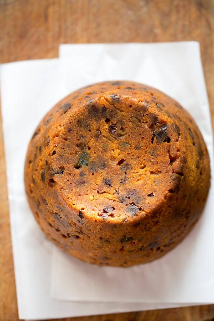 A whole boiled fruit cake on a white napkin with a wooden background.