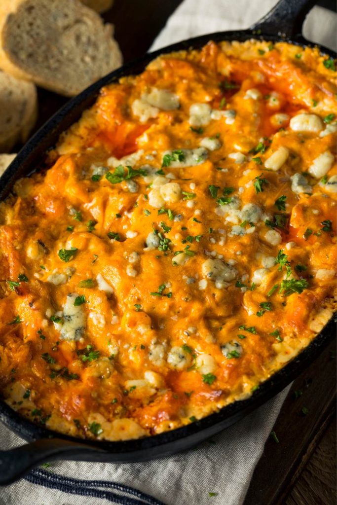 Buffalo chicken dip in a skillet, sprinkled with blue cheese and herbs.