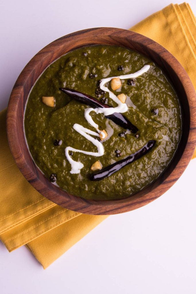 Wooden bowl of lamb saag garnished with cream and spices.