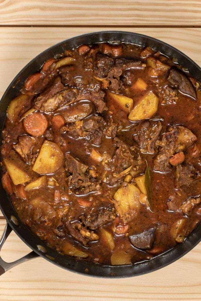 Close-up of slow cooker goat stew showing tender pieces of goat meat and diced vegetables.