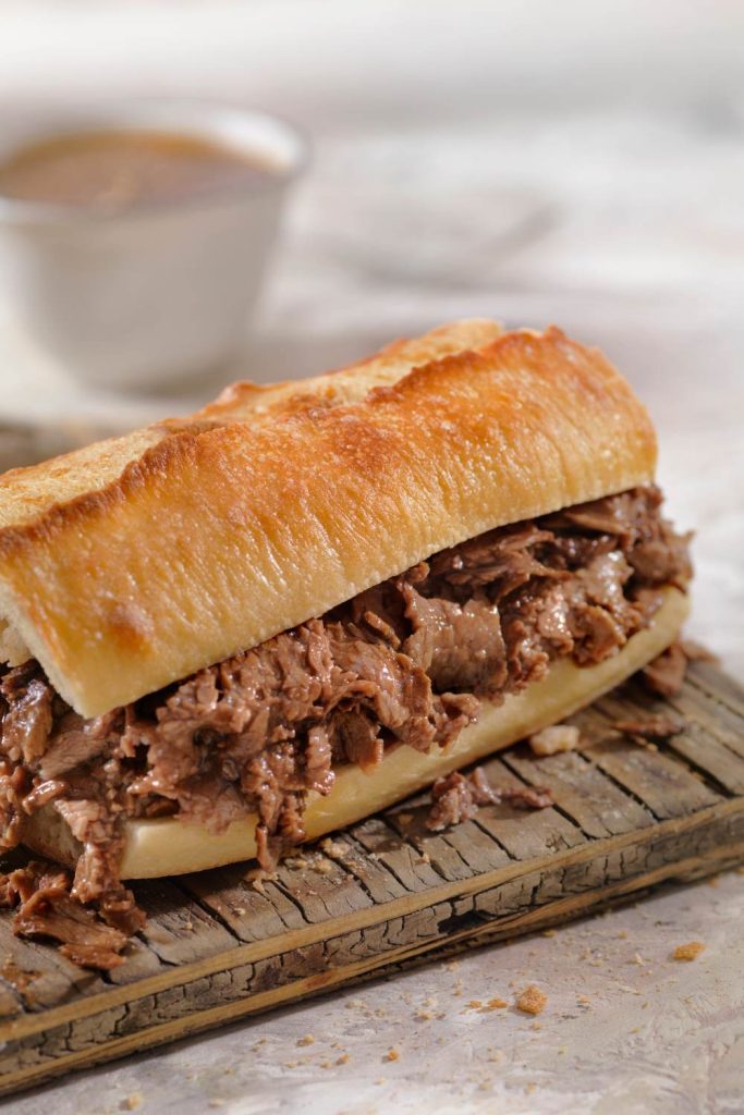 Beef sandwich on a cutting board with au jus dip.