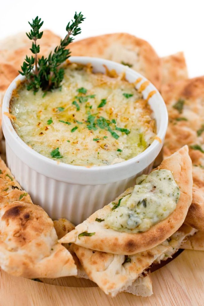 Slow cooked spinach and artichoke dip in a white bowl with bread around it.