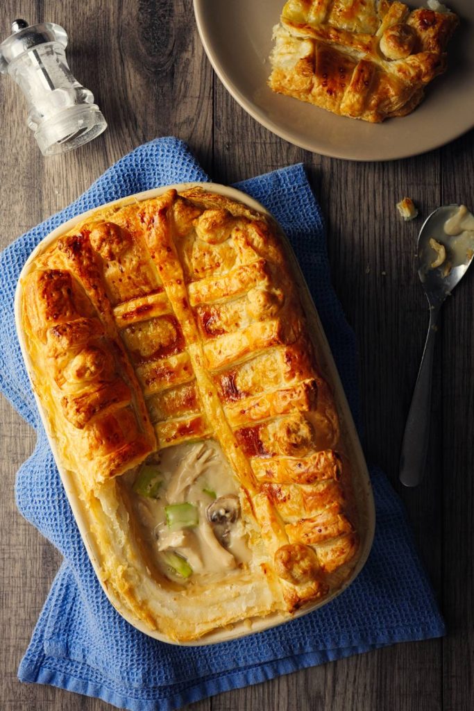 A whole chicken and leek pie with a golden pastry top in a ceramic dish.