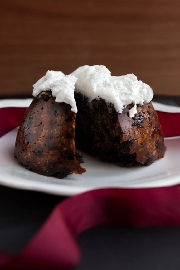 Two pieces of plum pudding topped with whipped cream on a plate.