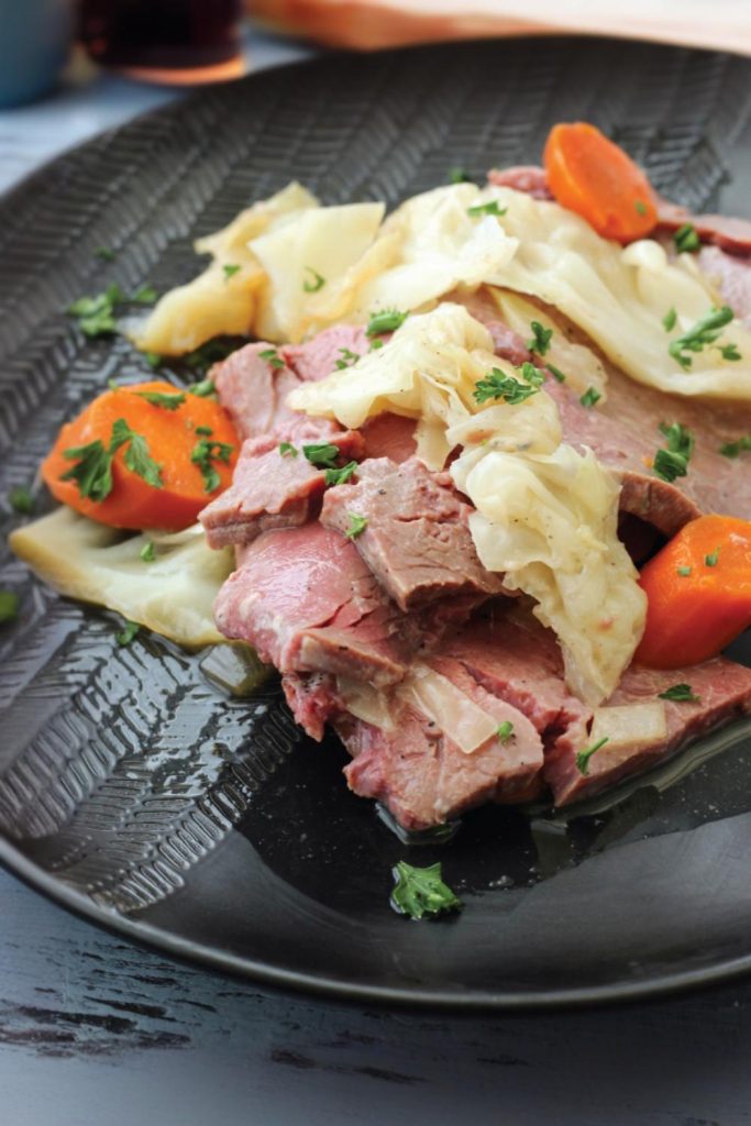A hearty serving of slow-cooked corned beef with vegetables on a textured black plate.