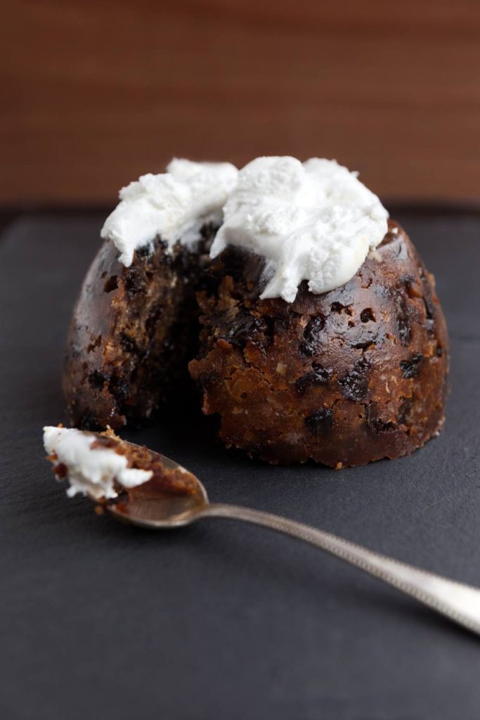 A single serving of plum pudding with a creamy topping on a slate background.