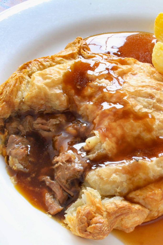 A serving of slow cooker steak pie with flaky crust and rich gravy.