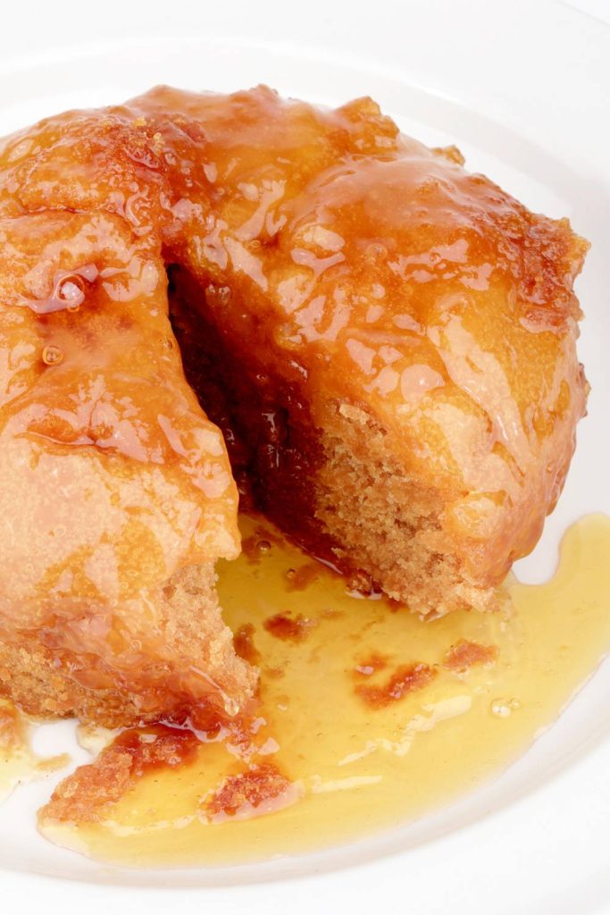 A piece of treacle sponge pudding with sticky sauce on a white plate.