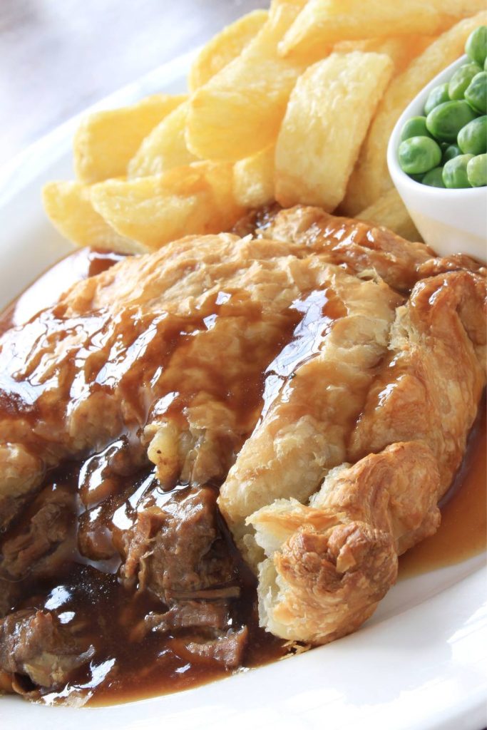 Steak pie with chips and peas, drizzled with gravy.