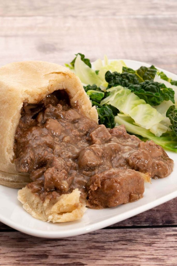 A plate with a cross-section of steak and kidney pudding, showing the meaty filling, served with green vegetables.
