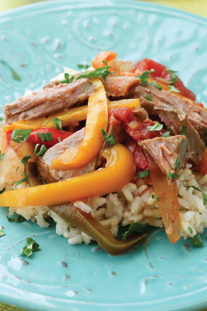 Tender slices of pepper steak with vibrant bell peppers over rice on a turquoise plate.