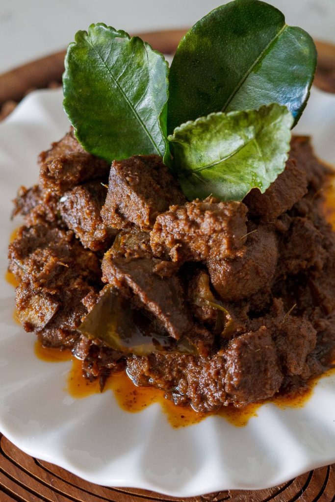 Plate of slow cooker beef rendang with leafy herbs.