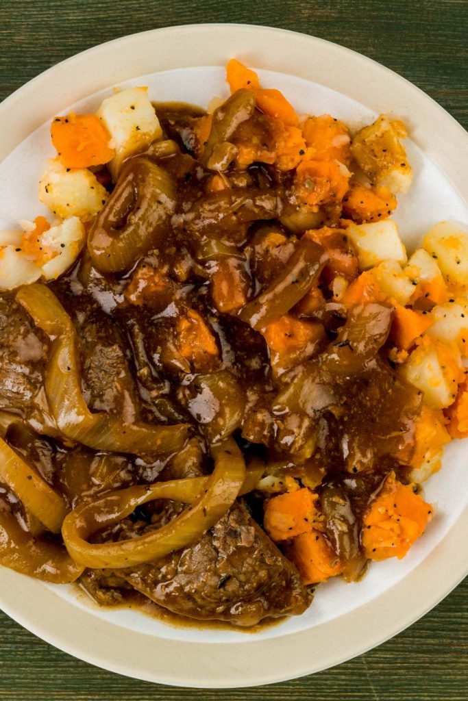 Plate of Slow Cooker Braised Steak and Onions with carrots and potatoes.