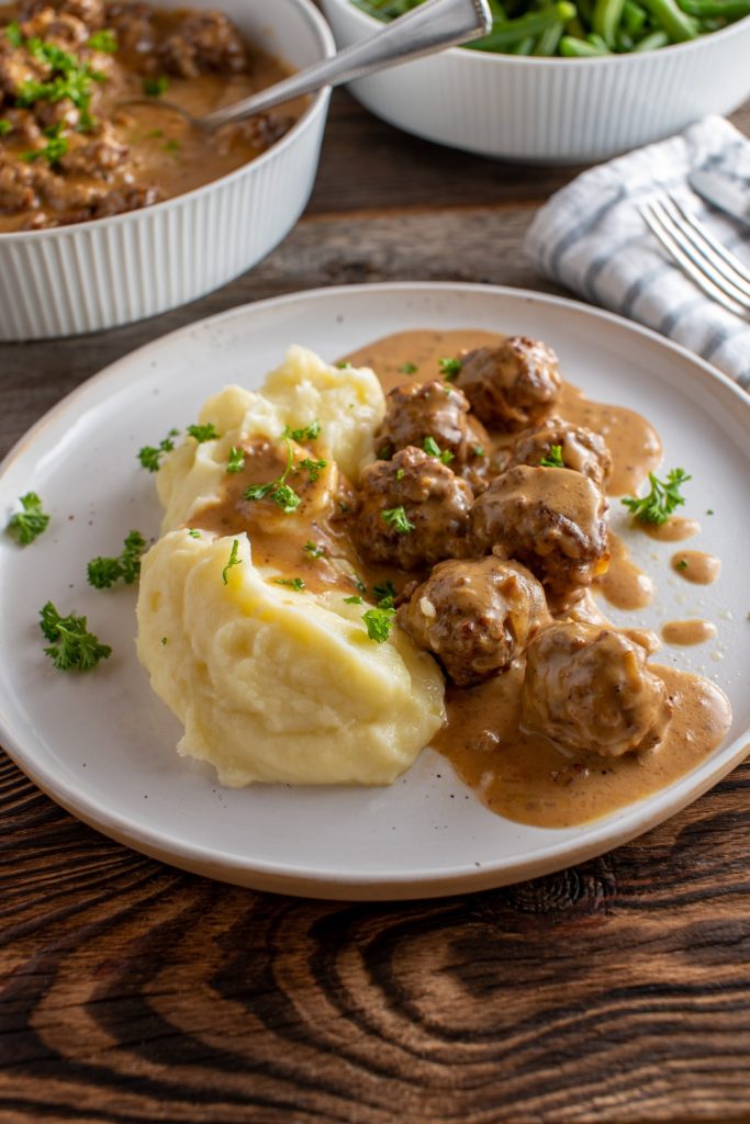 Slow Cooker Meatballs and Gravy served with mashed potatoes and green beans on a rustic table.