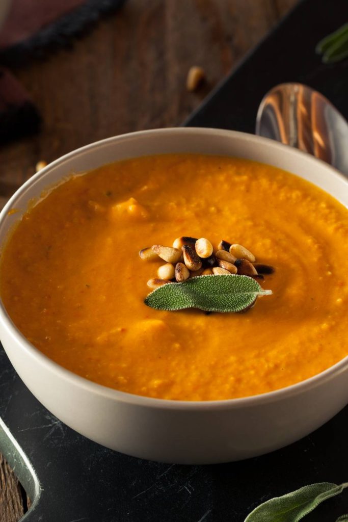 Thick carrot and parsnip soup in a white bowl with nuts and a green leaf on top.