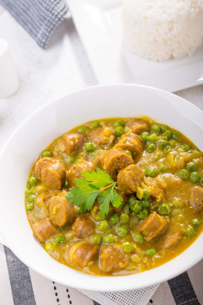 Curried sausages and peas in a white slow cooker bowl.