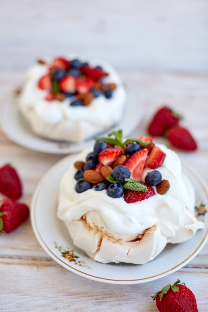 White pavlova with cream, strawberries, blueberries, and almonds on a plate.