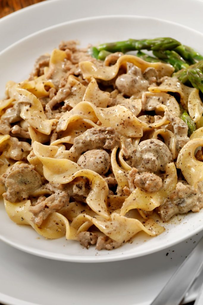 Beef stroganoff with noodles and asparagus on a white plate.