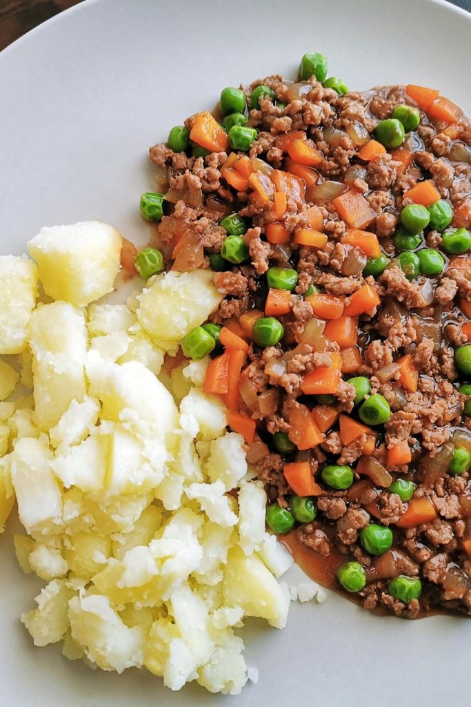 Close-up of mince meat with vegetables and mashed potatoes on a plate.