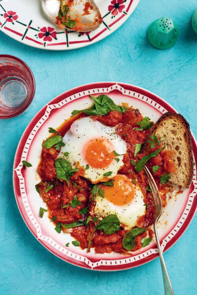 Slow Cooker Shakshuka with eggs and spinach on a decorative plate, with toast and a glass of water.