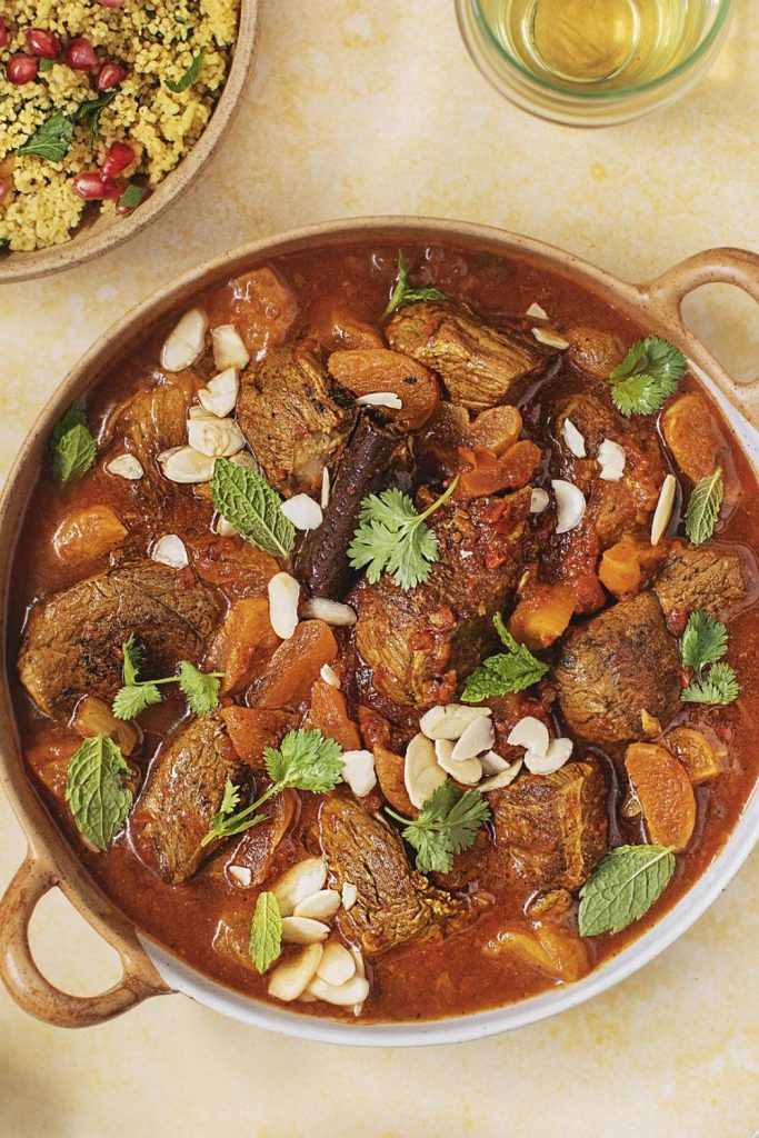 a Slow Cooker Spiced Apricot Lamb Tagine surrounded by sides and a glass of wine.
